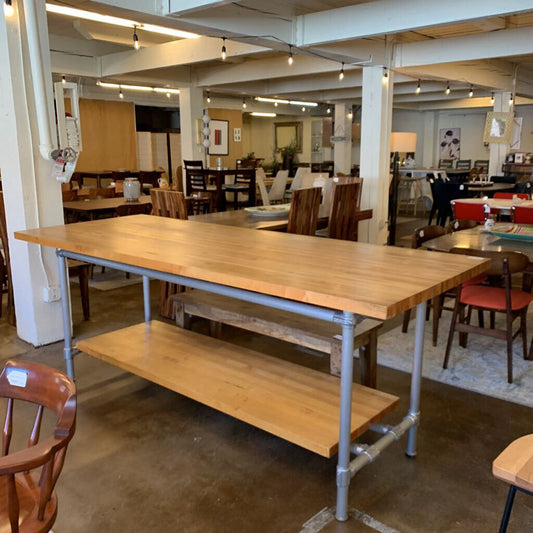 Long wooden table with metal legs in a room with chairs and tables.