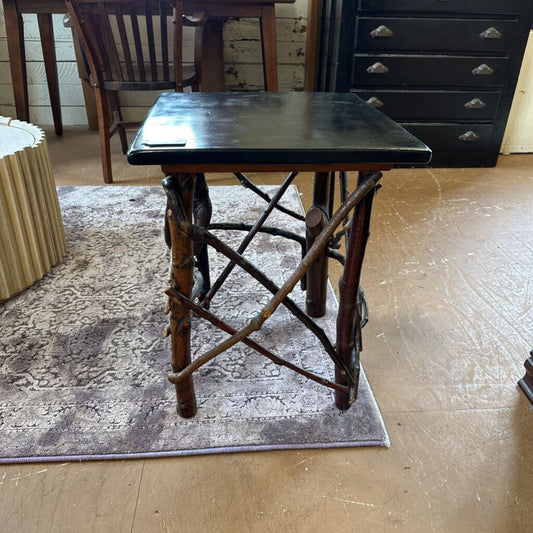 Small wooden table with a black top on a rug in a room with furniture.