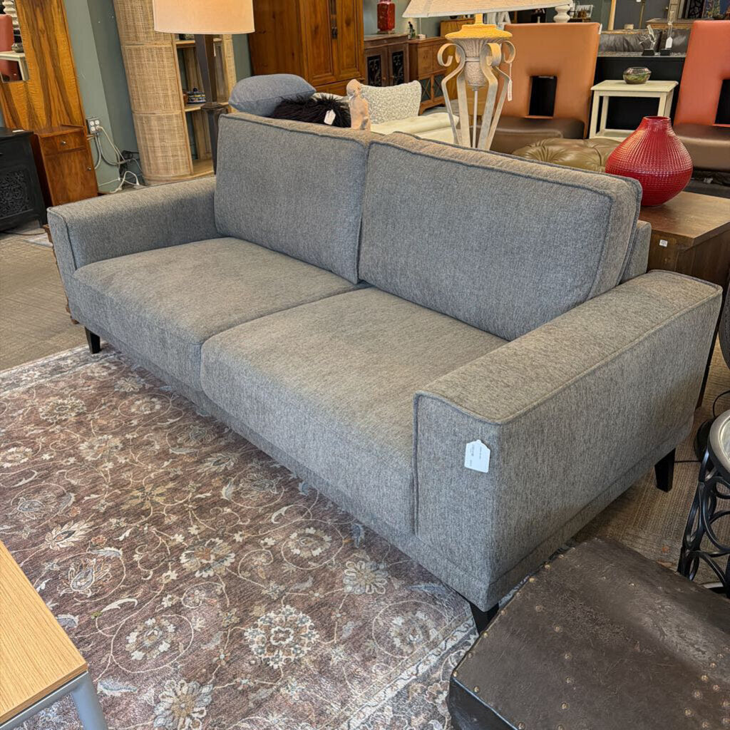 Gray sofa in a room with a patterned rug and various furniture pieces.