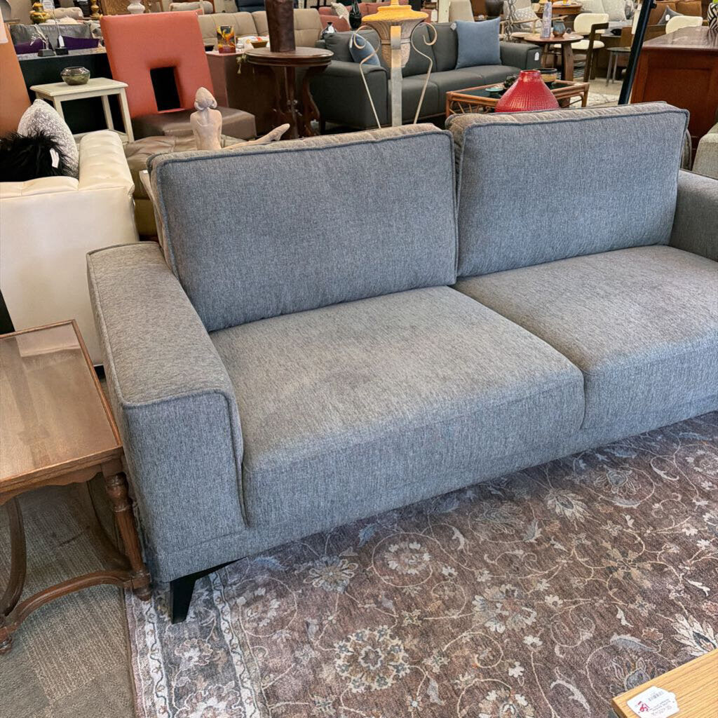 Gray sofa in a showroom setting with other furniture.