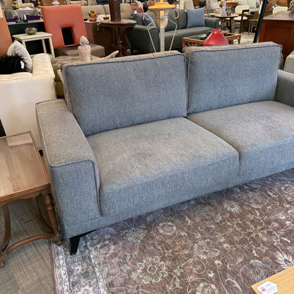 Gray sofa in a showroom setting with other furniture.