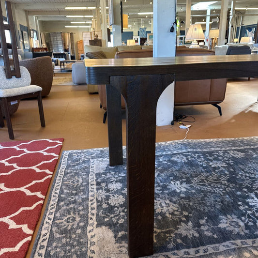 Dark wooden table in a furniture store with various chairs and a rug on the floor.