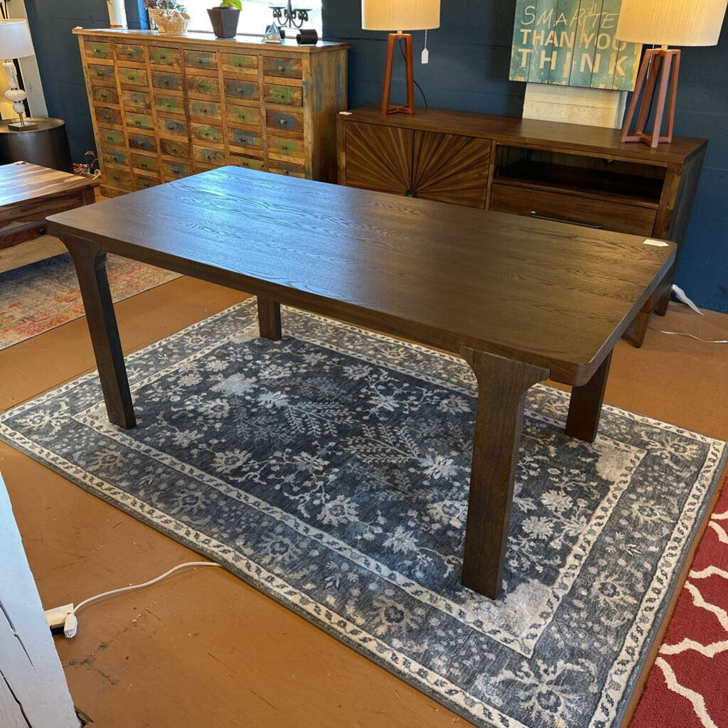 Wooden dining table in a room with a blue patterned rug and wooden furniture.