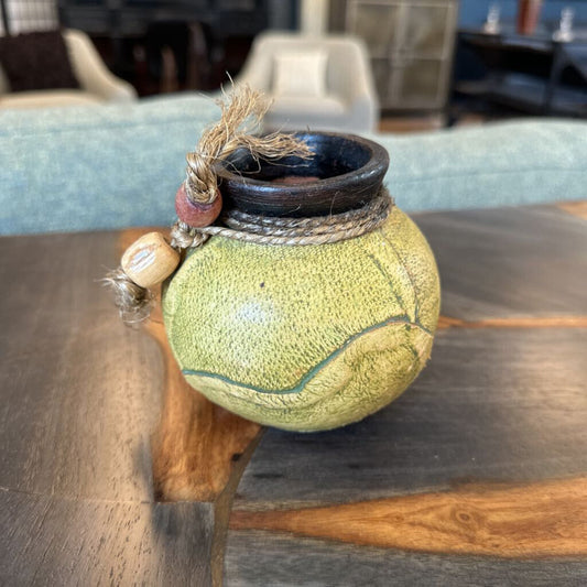 Decorative green ball with a small black pot on top, placed on a wooden surface.