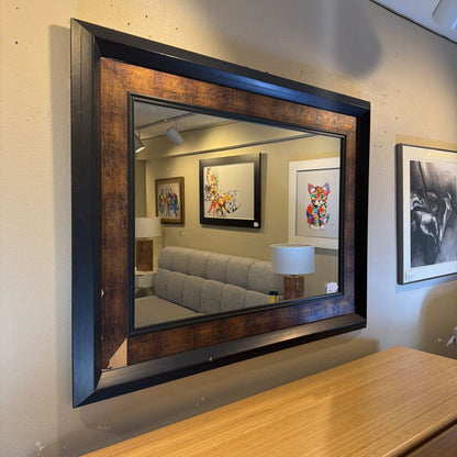 Large square mirror with a dark frame on a wall, reflecting a living room.