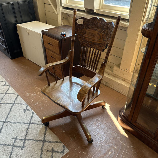 Wooden chair with armrests on a wooden floor in a room with a rug and furniture.