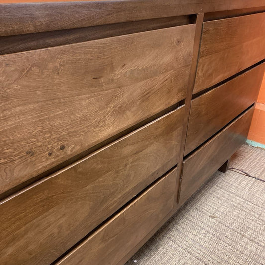 Wooden dresser with multiple drawers on a carpeted floor.