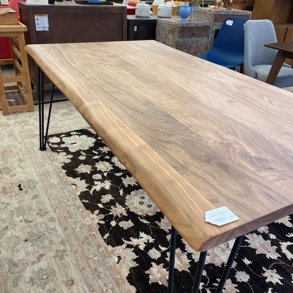 Wooden table with black metal legs on a patterned rug in a store setting