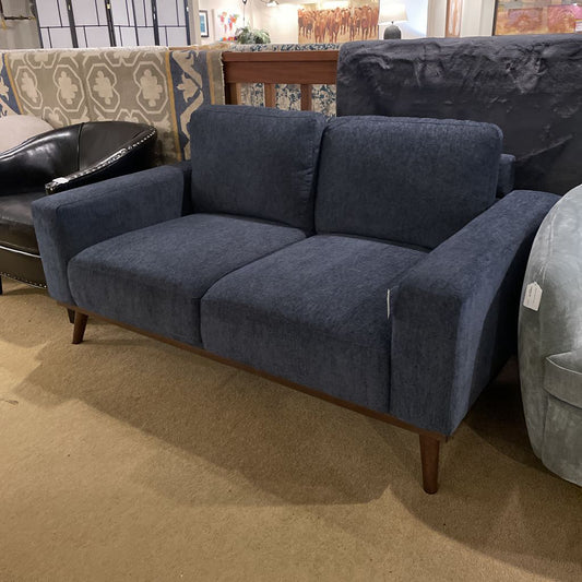 A two-seater loveseat with navy blue textured upholstery, two back cushions, and tapered wooden legs