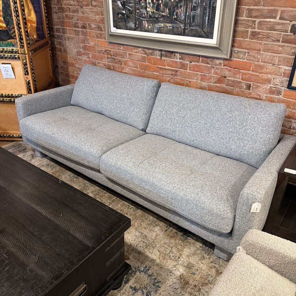 Gray sofa in a room with a brick wall and framed pictures.