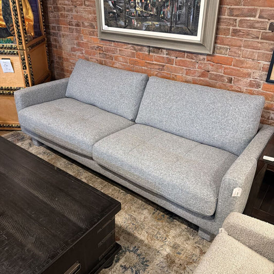 Gray sofa in a room with a brick wall and framed pictures.