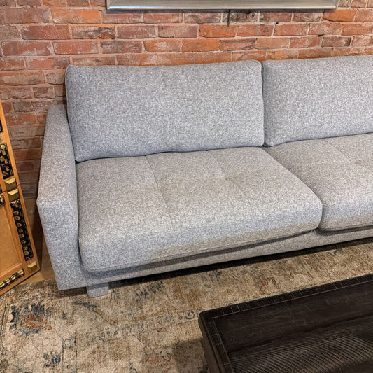 Gray sofa against a brick wall in a room with a rug and wooden cabinet.