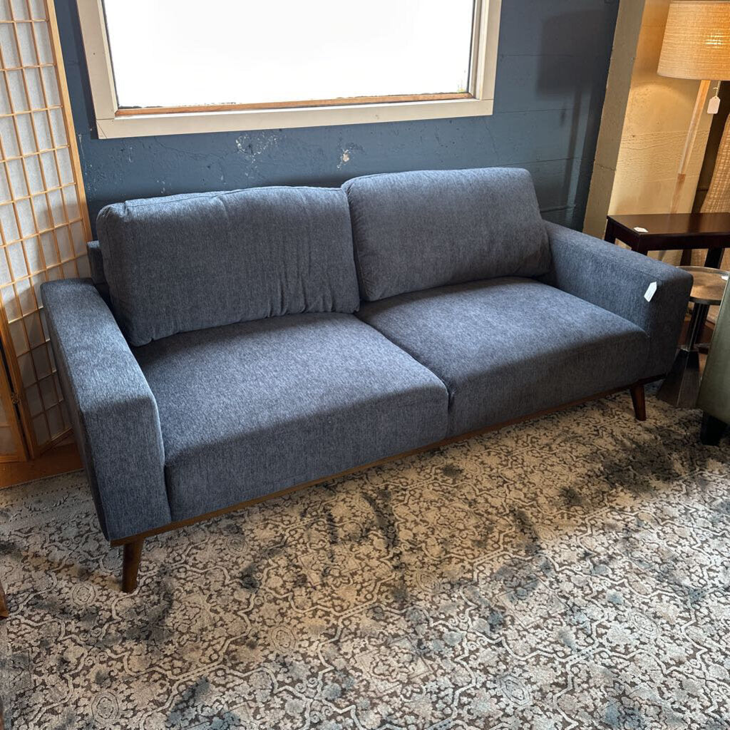Gray sofa in a room with a patterned rug and window.