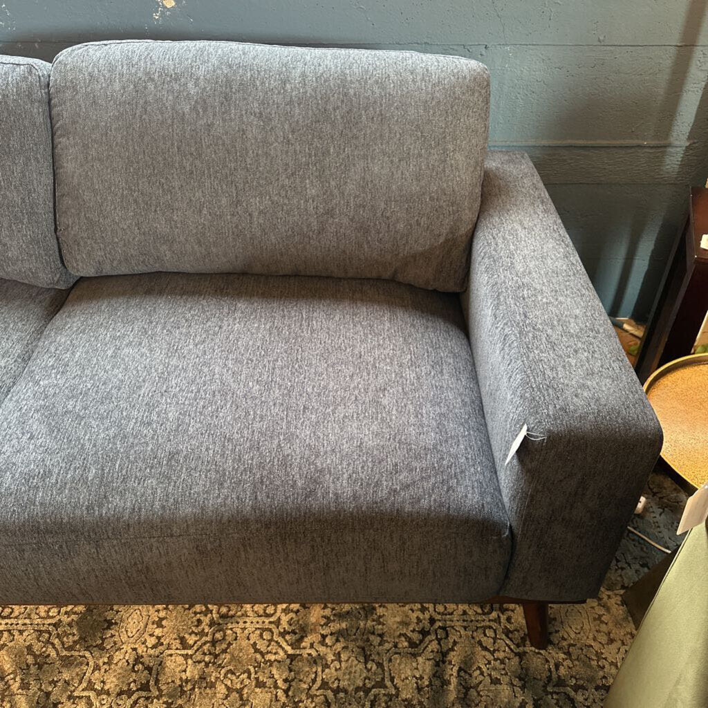 Gray sofa in a room with a patterned rug and wooden floor.