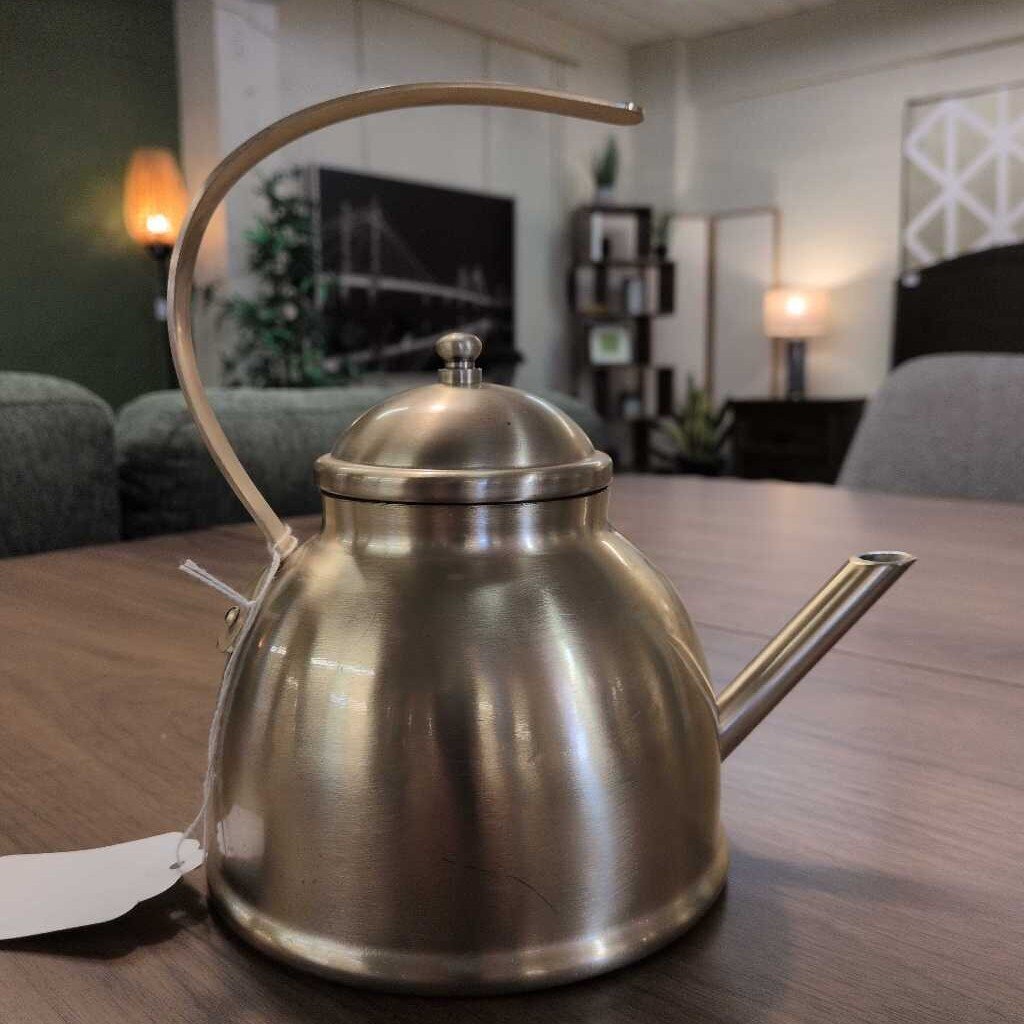 Stainless steel kettle on a wooden table with a blurred indoor background