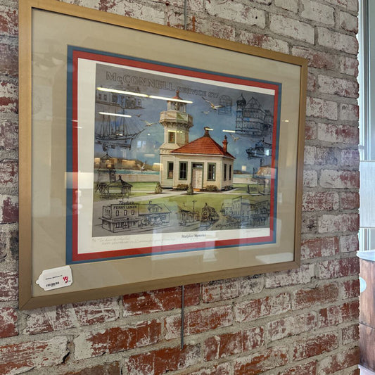Framed artwork of a lighthouse scene on a brick wall