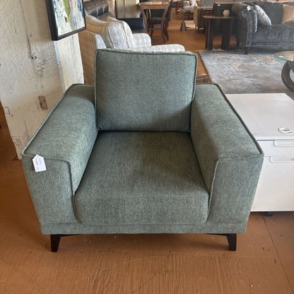 Gray armchair in a showroom setting with other furniture in the background