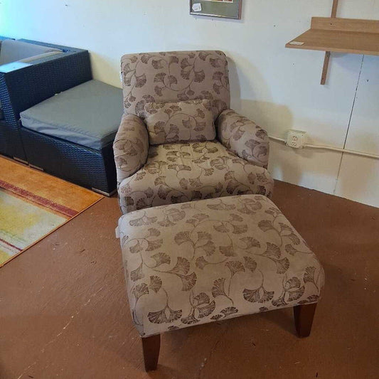 Patterned armchair and ottoman on a wooden floor with a wall socket in the background.