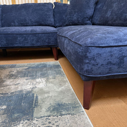 Blue sectional sofa in a room with a textured rug on the floor.