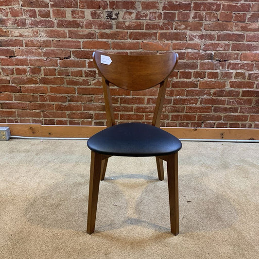 Wooden chair with black seat against a brick wall.