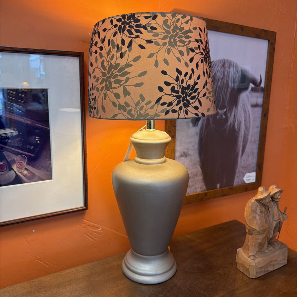 Decorative lamp with floral patterned shade on an orange wall with framed pictures.