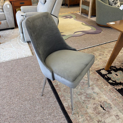 Gray upholstered chair in a furniture store setting with other chairs and a rug.