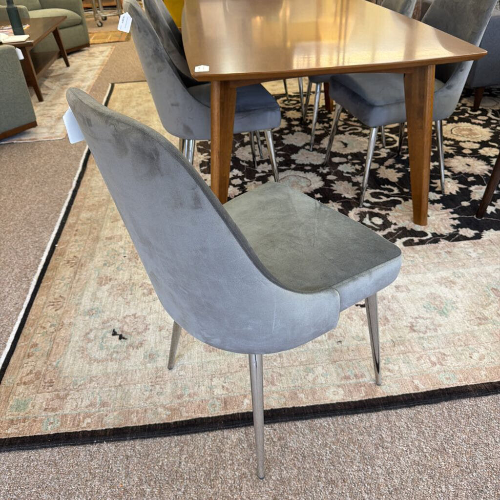 Gray chair in a furniture store setting with a wooden table and other chairs.