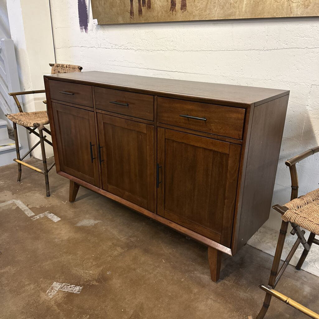 Wooden sideboard with drawers and doors in a room with chairs and a painting.