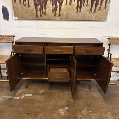 Wooden sideboard with open doors in a room with chairs and a painting on the wall.