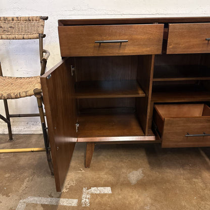 Wooden sideboard with open cabinet door and drawers on a concrete floor.