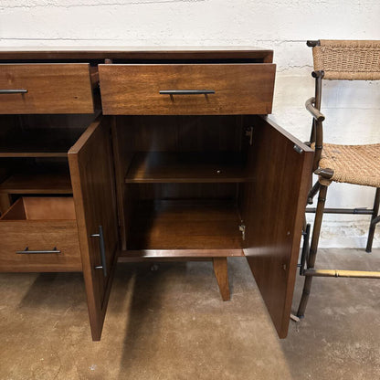 Wooden sideboard with open doors and drawers in a room setting.