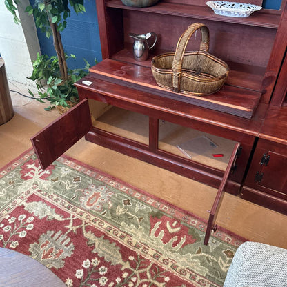 Wooden sideboard with open door displaying a basket on a patterned rug.