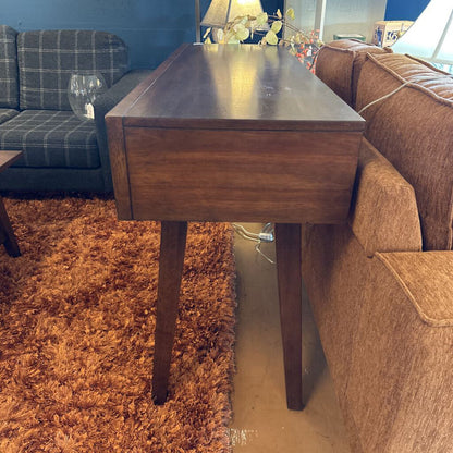 Wooden side table in a living room with brown sofa and plaid armchair.