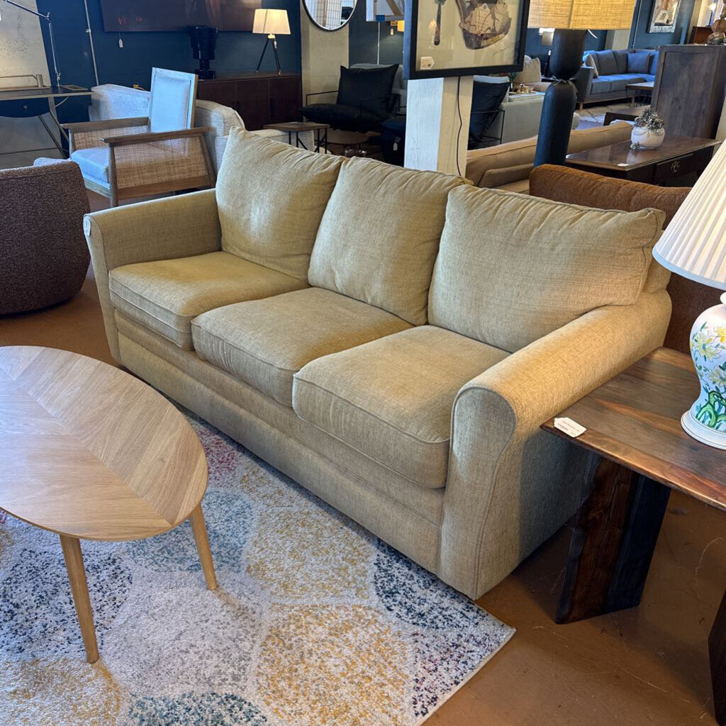 Beige sofa in a living room setting with tables and decor.