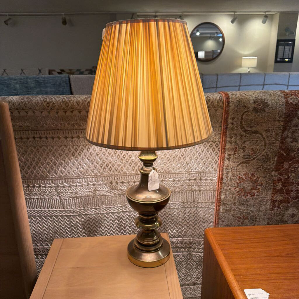 Table lamp with a gold shade on a wooden table against a patterned wall.