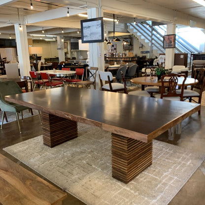 Large wooden dining table in a showroom with chairs and other furniture.