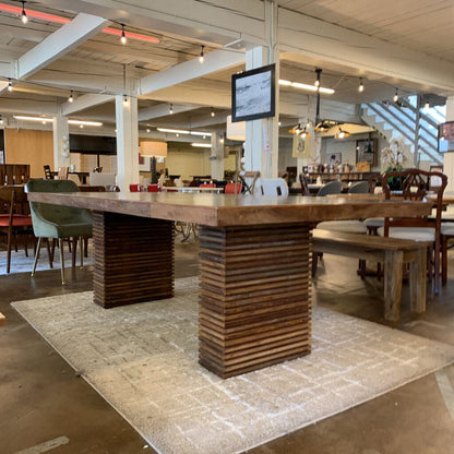 Large wooden table in a modern indoor setting with chairs and a TV screen in the background.