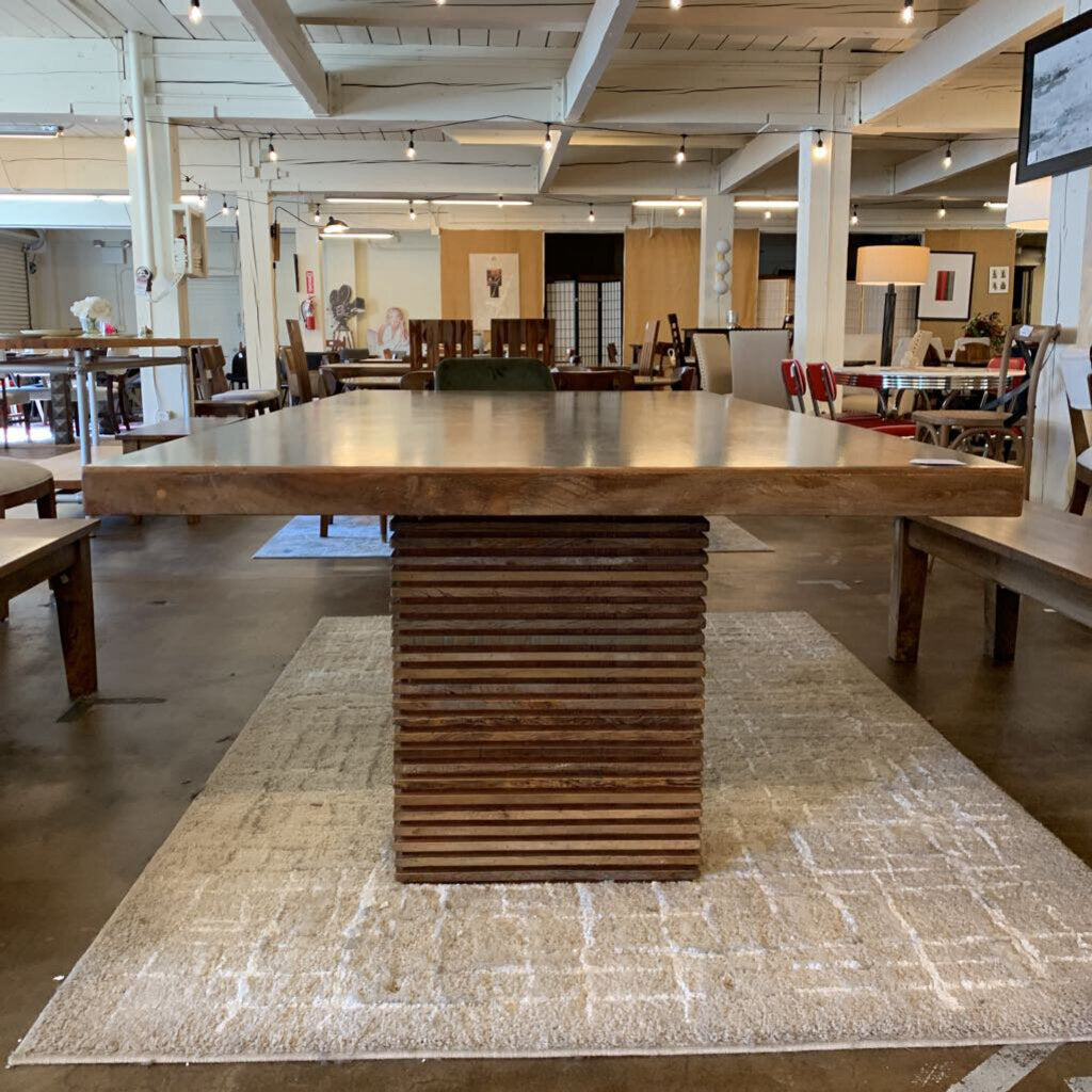 Large wooden dining table in a showroom setting with other furniture and decor.