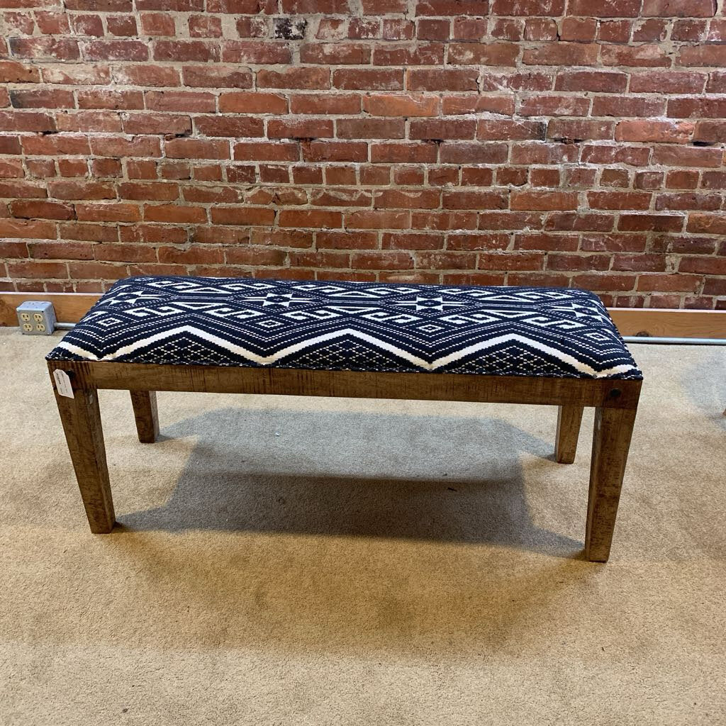 Wooden bench with a blue and white patterned cushion against a brick wall.
