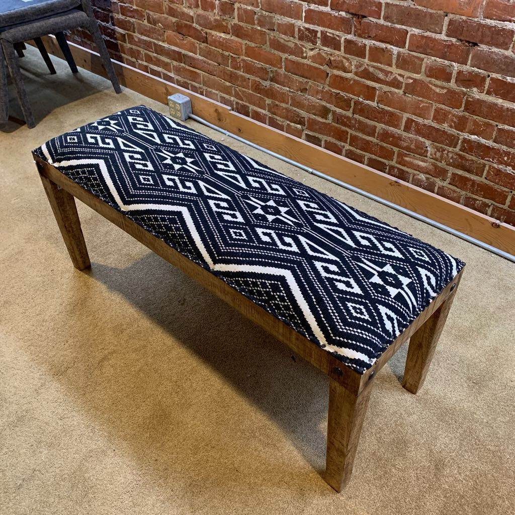 Wooden bench with a blue and white patterned cushion against a brick wall.