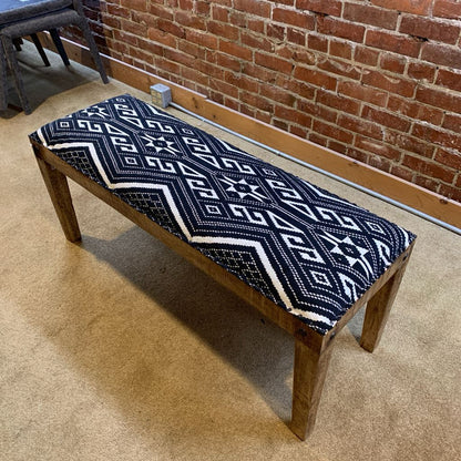 Wooden bench with a blue and white patterned cushion against a brick wall.