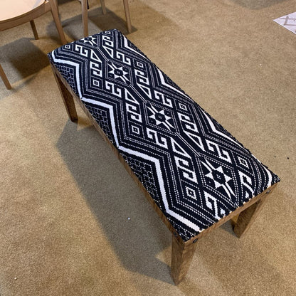 Wooden bench with a black and white patterned cushion on a beige carpet.