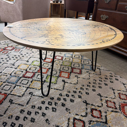 Round wooden table with hairpin legs on a patterned rug in a room setting.