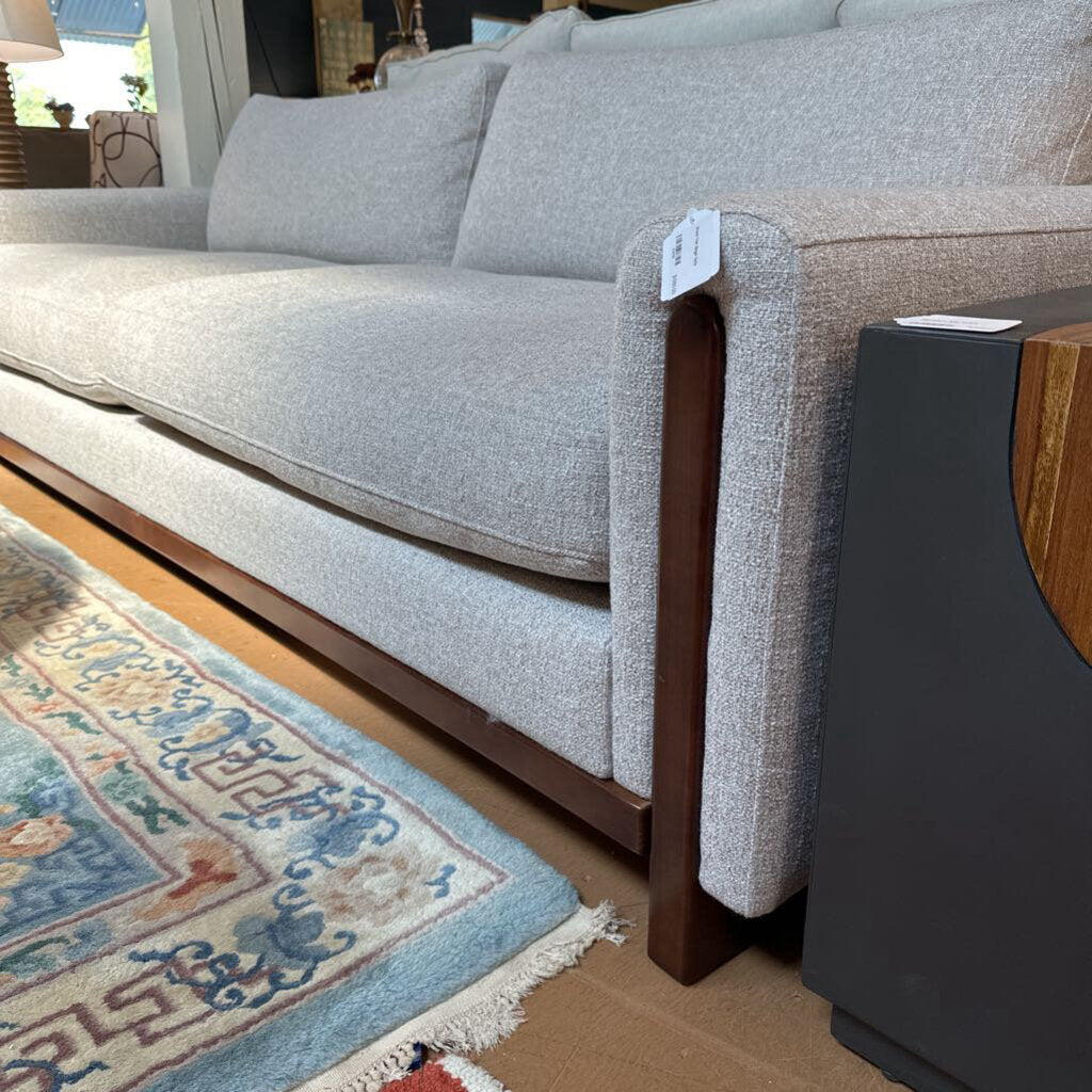 Gray sofa with wooden armrests on a wooden floor next to a patterned rug.