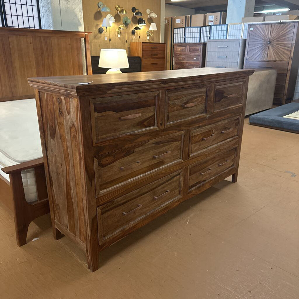 Wooden dresser in a furniture store setting with other furniture items in the background.