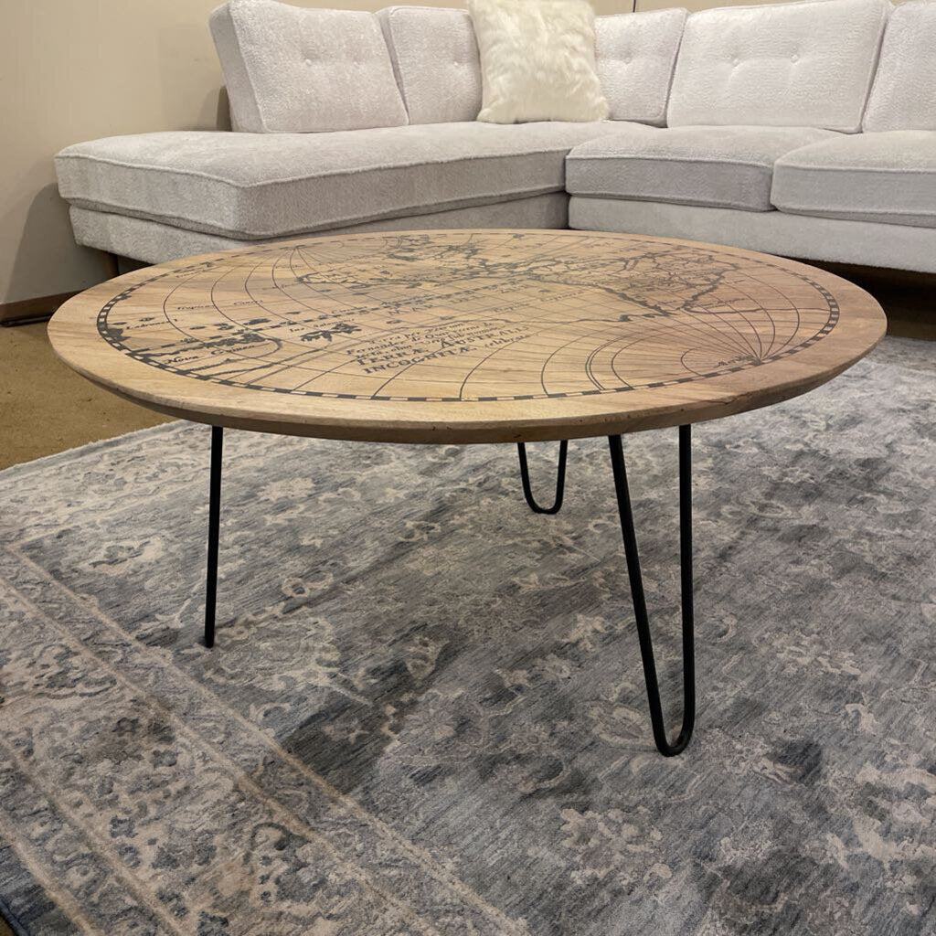 Round wooden table with decorative design on a rug in front of a gray sectional sofa.