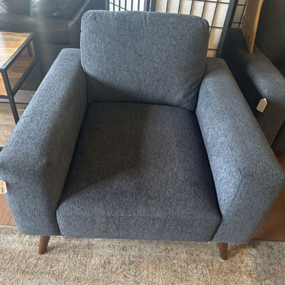 Gray armchair in a room with a rug and part of another chair visible.