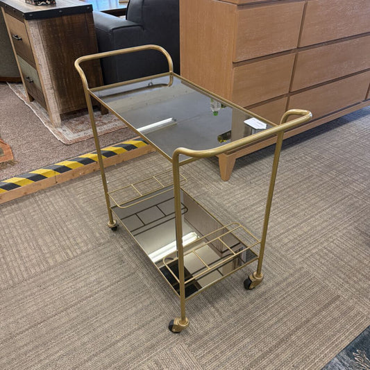 Gold metal serving cart on a carpeted floor with furniture in the background