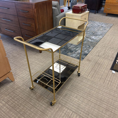 Gold bar cart with black glass shelves in a room setting