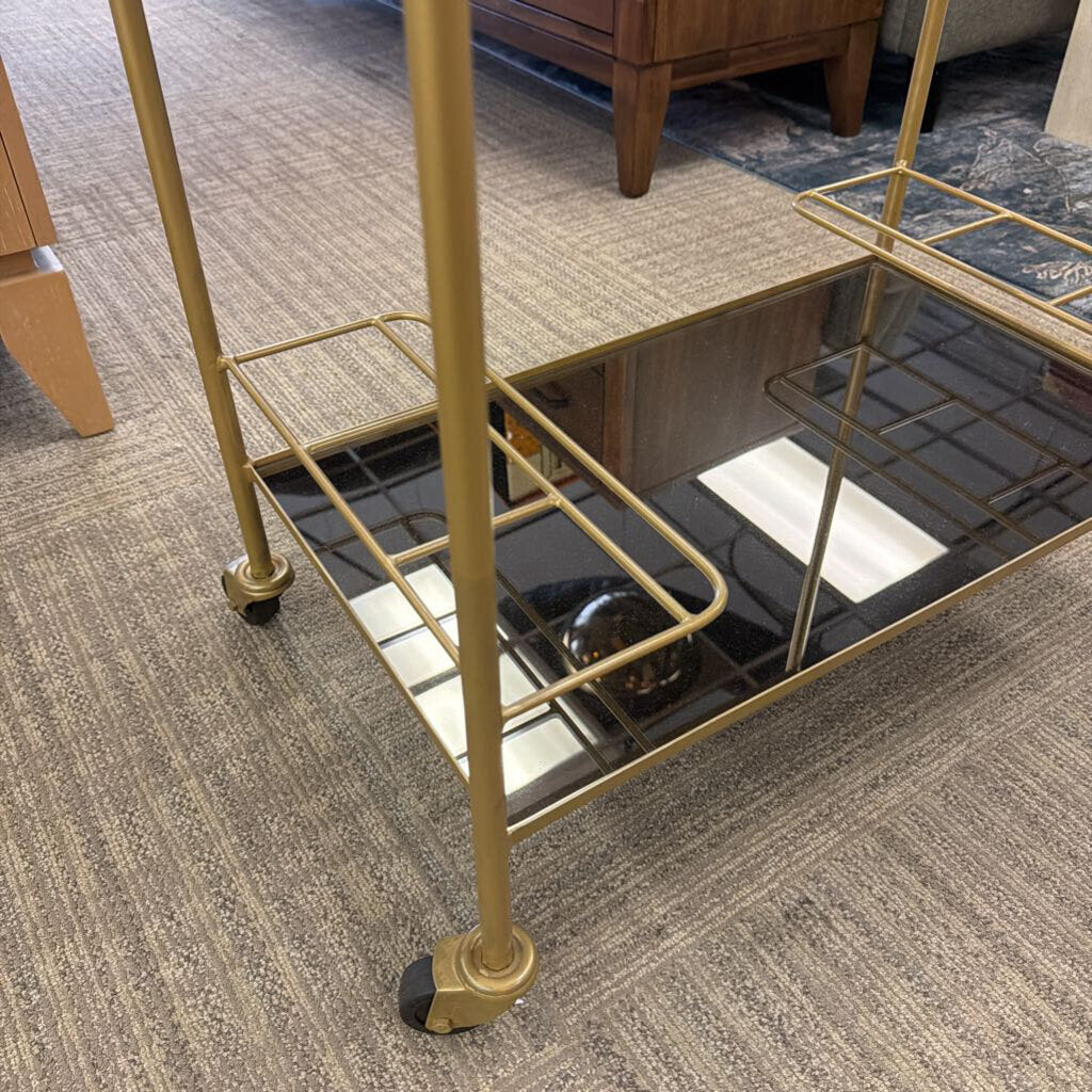 Gold metal bar cart with glass shelves on a carpeted floor